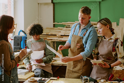 Картината върху платно Teenagers studying woodworking, reviewing plans and taking notes during vocational class in workshop