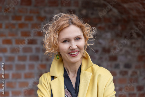 Close up portrait of smiling middle aged woman with curly hair and yellow coat