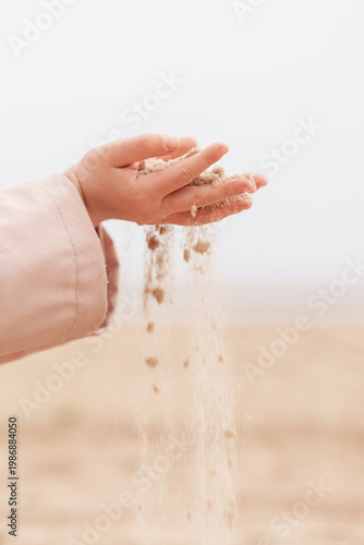 Obraz na płótnie Child hands pouring dry sand on a wide beach, sensory play, childhood exploration, coastal background