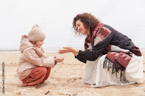 Photos Woman showing seashells to a little girl while sitting on a sandy beach, educational moment, motherly care, seaside discovery