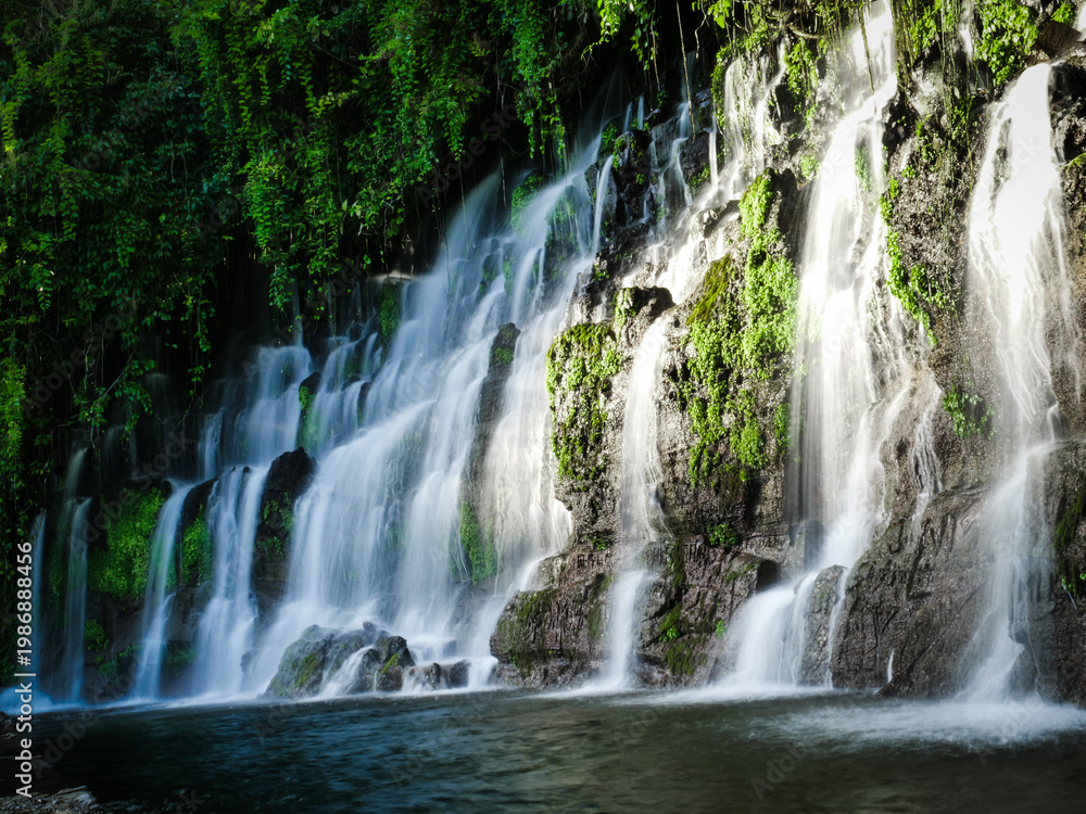 Obraz premium Lush green moss-covered rocks cascade with a vibrant waterfall creating a tranquil natural scene