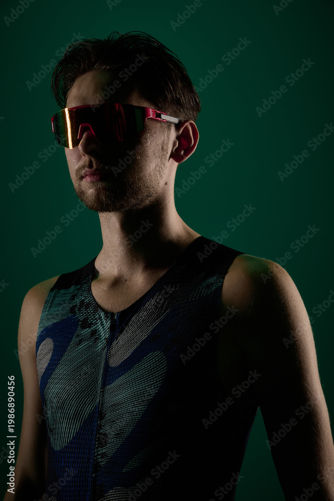 Fototapeta premium Close up portrait of male athlete wearing sports sunglasses on dark green background. Concept of sport fashion visuals, performance gear promotion, active lifestyle branding, fitness identity content.