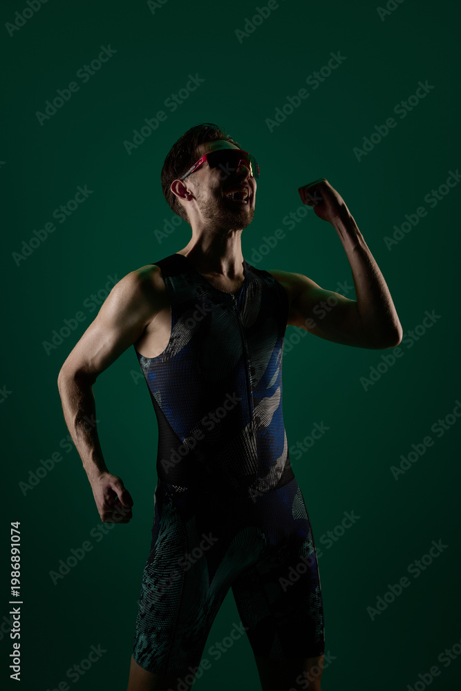 Fototapeta premium Male athlete celebrating with clenched fist and raised arm in studio lighting. Concept of winning moment visuals, success celebration content, motivation energy, achievement and confidence.