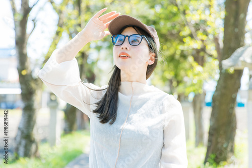 サングラスでUV対策する屋外の女性　
Young woman protecting from UV rays outdoors in park wearing sunglasses and cap sun protection portrait lifestyle