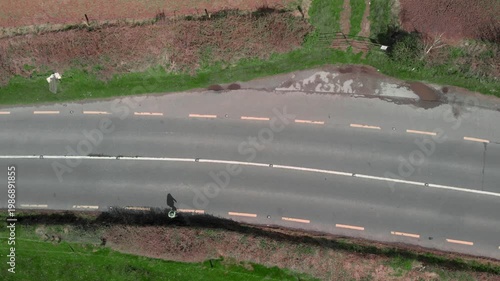 Person walking alone on narrow rural road shoulder, highlighting lack of sidewalks and safety concerns, conveying infrastructure challenges and pedestrian vulnerability for urban planning and public s