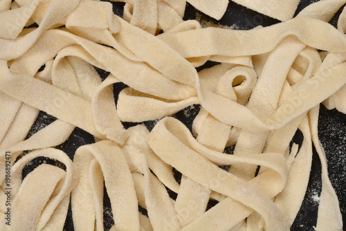 фотографія Top view of raw homemade tagliatelle pasta scattered over a black floured surfac