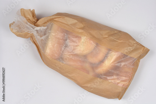 Foto A brown paper bakery bag with a transparent plastic window filled with several golden brown bread rolls on a white background