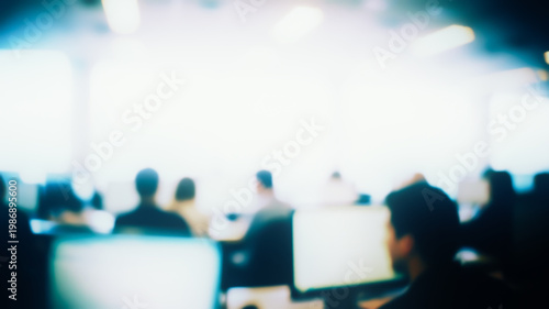Heavily blurred abstract background of a modern open-space office, where silhouettes of people work behind computer monitors