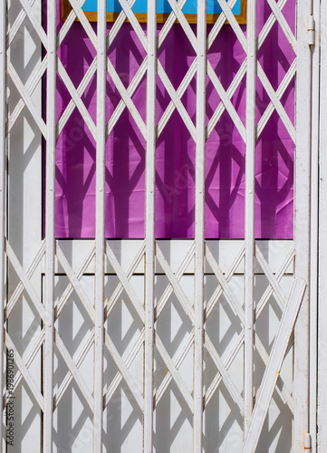 Closed shop entrance with white metal security gate casting geometric shadows on colorful background with strong contrast