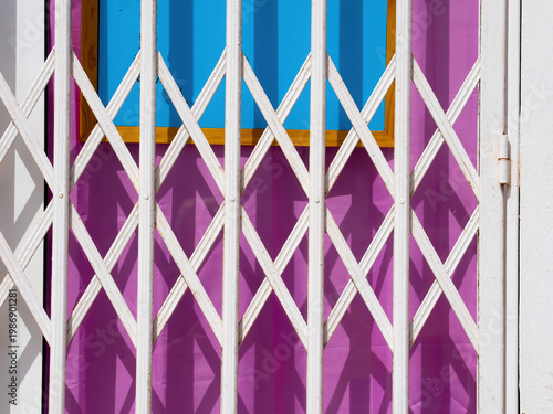 Closed shop entrance with white metal security gate casting geometric shadows on colorful background with strong contrast