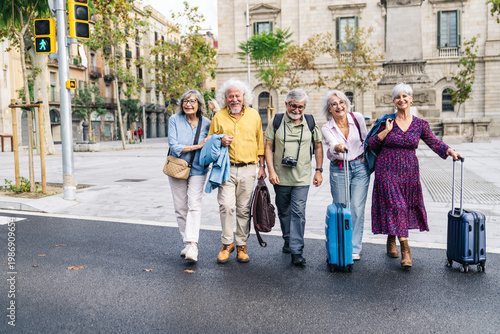 Group of smiling mature friends walking on street with luggage, enjoying their retirement travel and urban tourism lifestyle