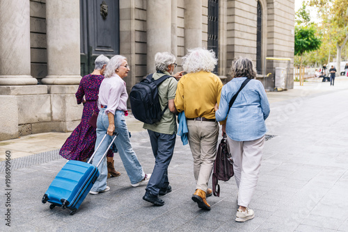 Group of senior adults enjoying active retirement, walking with luggage through a city, exploring a new destination