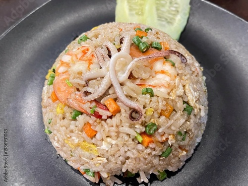 Authentic Thai seafood fried rice topped with shrimp and squid, served with fresh vegetables and vibrant flavors.