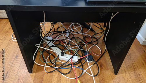 A cluttered computer desk with tangled wires and cords