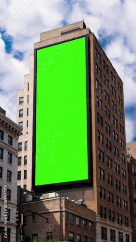 Green chroma key blank vertical billboard mock up in city center for advertising on apartment with beautiful clouds background