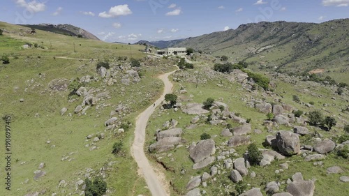Drone lowers over hiking trail and two hikers climb the hill on a sunny day at Sibebe Rock near Mbabane, Eswatini