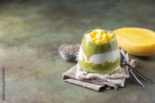 Chia pudding on coconut milk with matcha tea, mango slices and yoghurt in a glass. Healthy eating