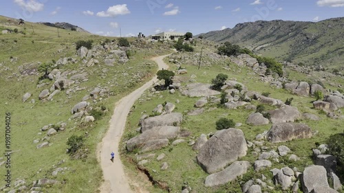 Drone flies over hikers on trail heading toward building on a sunny day at Sibebe Rock near Mbabane, Eswatini