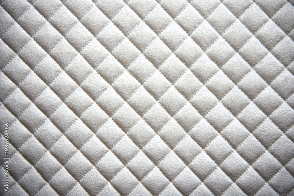 Fototapeta premium White quilted fabric with a diagonal diamond pattern.