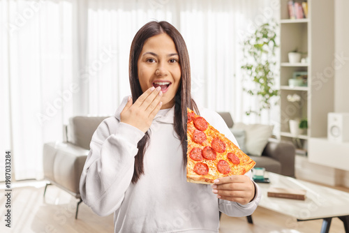 Young surprised woman holding a slice of pepperoni pizza