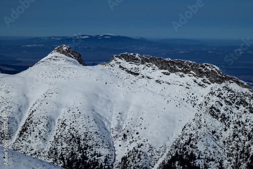 Mountains covered in snow with a clear blue sky and distant hills visible during daytime in winter season. Tatra Mountains. View of Giewont Peak. Poland. Zakopane