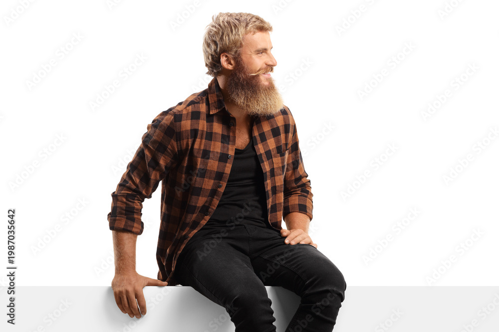 Obraz premium Young bearded man sitting on a white panel board and looking to the side