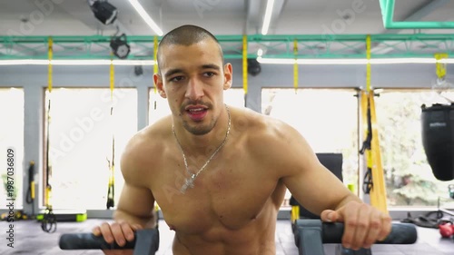 Athletic man engaged in intense workout on fitness machine, showcasing determination and strength, with gym environment highlighting equipment and active atmosphere, emphasizing physical fitness