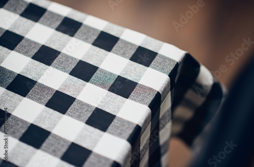 Close up of a black and white checkered cafe tablecloth draped over the edge of a table, the bold monochrome pattern creating a clean look at the coffee shop.