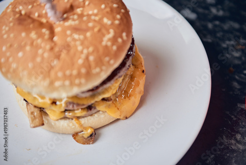 Close up of a cheeseburger in a takeaway container set on a black and white checkered tablecloth, with warm golden bun tones and melted cheese. Classic uk cafe culture.