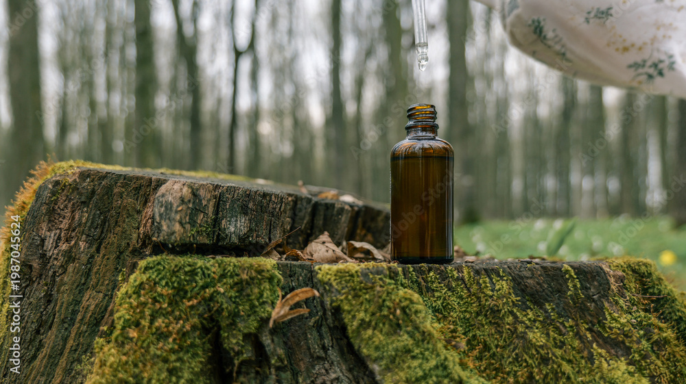 Naklejka premium Amber glass dropper bottle with liquid on mossy tree stump in forest