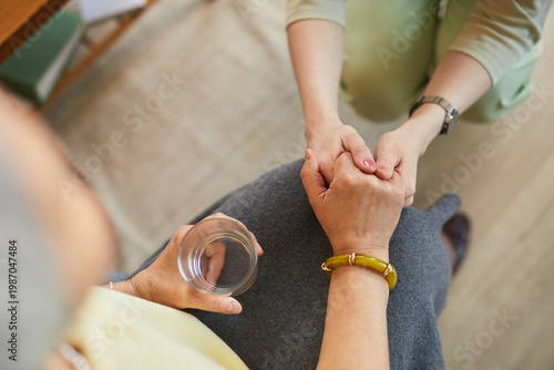Photos Senior woman receiving supportive handhold from female caregiver in nursing home