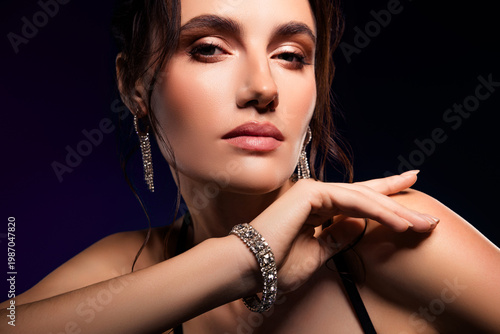 Magnificent young woman with dark hair wearing glamorous jewelry posing stylishly against dark background