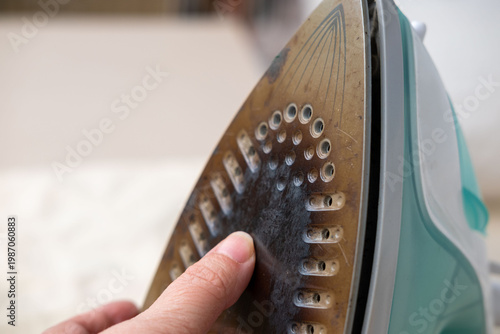 burnt black iron with scorched fabric residue, worn-out iron soleplate, damaged household appliance, Stains and scratches, overheating accident, domestic failure, caution and safety, appliance failure