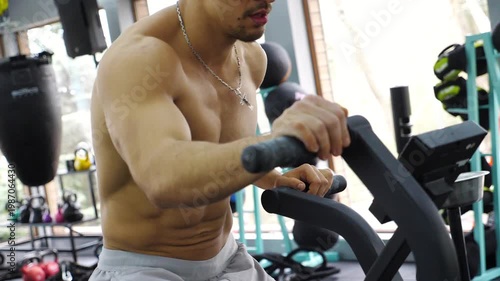 Male fitness enthusiast engaged in intense workout on exercise bike, showcasing determination and focus in a modern gym environment with vibrant equipment and natural light streaming through windows