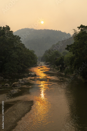 Peaceful sunset landscape over calm river surrounded by lush green forest and scenic mountain reflecting warm sunlight rippling water creating serene relaxing atmosphere beautiful quiet nature