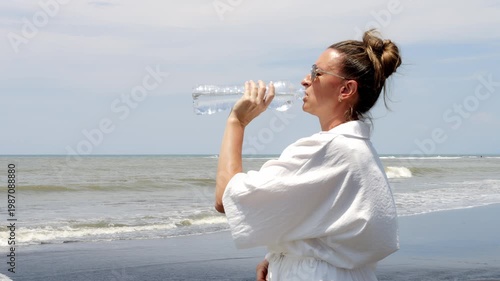Awareness on sunny beach woman drinking water to prevent dehydration under strong sun Hydration protects body from heat stress hydration supports balance hydration becomes essential daily habit