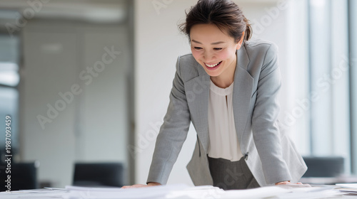 会議室のテーブルに手をついて笑顔で資料を確認するビジネスウーマン
