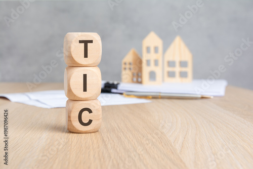TIC - Tenancy in Common - acronym on wooden blocks. Blurred background with miniature houses. Real estate concept.