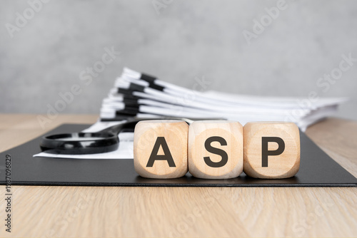 ASP acronym on wooden blocks. Blurred background with a document stack and magnifying glass. Business and finance concept.