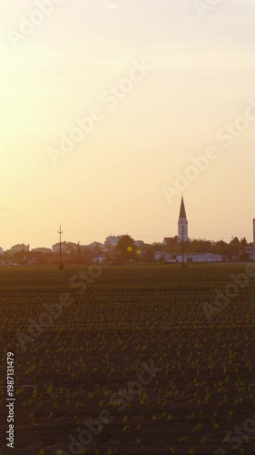 Driving beside a farm field with city and sunset in background
