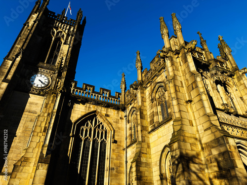 Gothic church and clock tower facade in Manchester, UK bathed in golden light against a deep blue sky