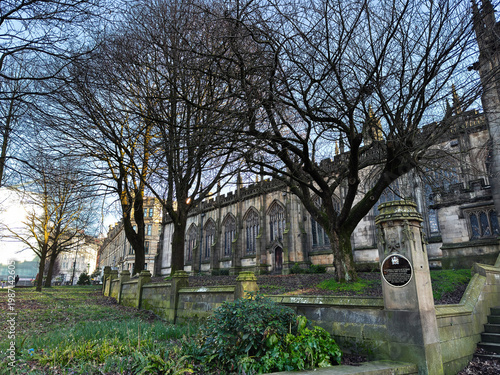 Historic cathedral in Manchester, UK framed by bare winter trees, mossy stone walls, arched gothic windows and tranquil churchyard atmosphere