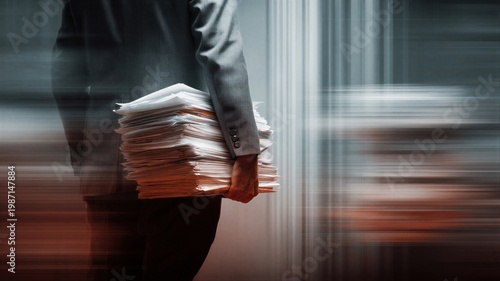 Man employee in suit carrying heavy stack of paper documents in office. Concept of corporate drudgery, overwork and burnout. Professional pressure and high workload in business environment.