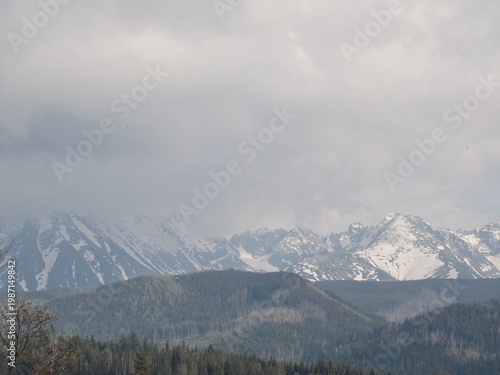 Tatra Mountains landscape featuring snow-capped peaks and lush green valleys under a cloudy sky in Zakopane, Poland, showcasing natural beauty and rugged terrain