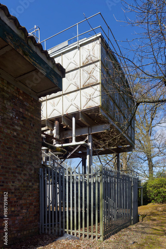 A side and back view of the Historical Steel Water Tanks at Stracathro Hospital Entrance, with a brick built workshop and metal railing fence.