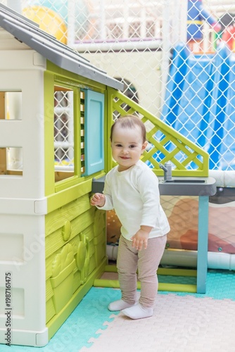 Happy toddler playing near toy kitchen and playhouse in daycare