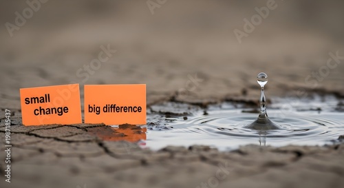 A single raindrop creates ripples in a dry, cracked mud puddle with inspirational signs reading small change big difference.