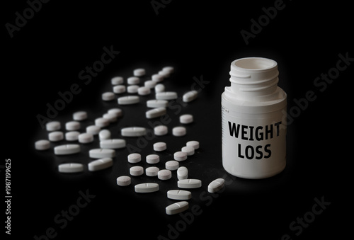 Different weight-loss drug tablet pills with container on black background. Concept image with shallow depth of field.