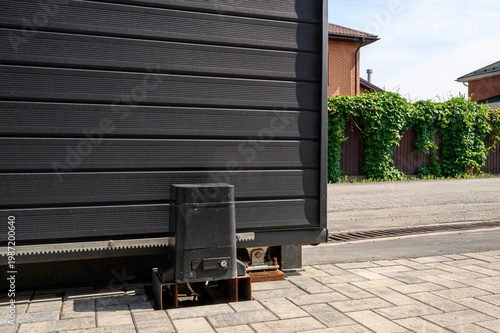 Foto black sliding gate with an automatic drive mechanism, mounted on a paved area