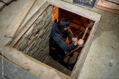 Man descending metal ladder into a cellar through a floor hatch in a utility room, showing access to underground storage space.